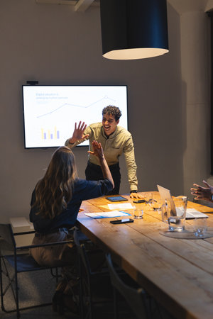 High-fiving during successful presentation, business professionals in modern conference room....