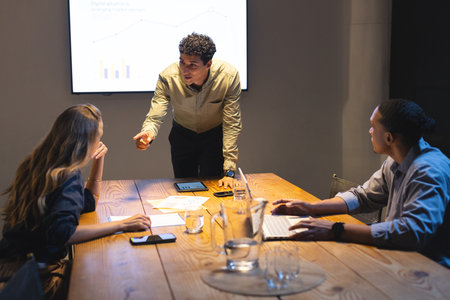 Businessman presenting data to colleagues in conference room during evening meeting. teamwork,...