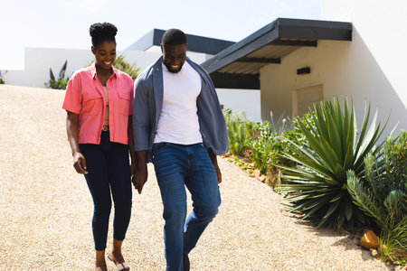 Couple walking outdoors on sunny day, enjoying time together and smiling. happiness, relationship, romance, leisure, bonding, togethernessの写真素材