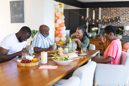 Family celebrating retirement with laughter and food around dining table at home. Celebration,...