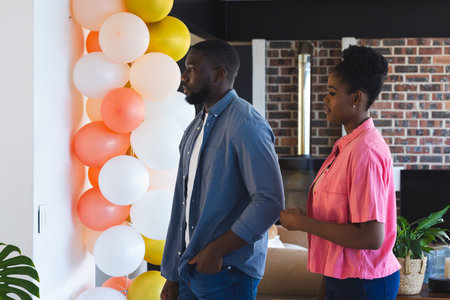 Couple admiring colorful balloon decorations at home, enjoying festive atmosphere. Celebration,...