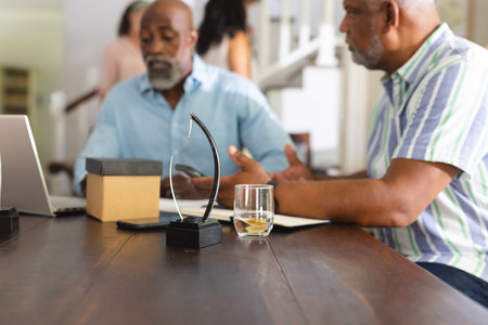 African American men discussing business at home with laptop and award on table. Diversity,...