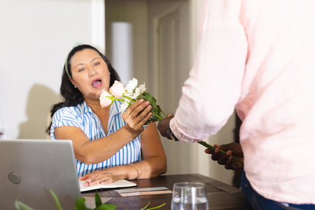Receiving flowers, surprised woman at home with laptop, expressing gratitude and joy. celebration, happiness, bouquet, appreciation, online, virtualの写真素材