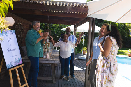 Celebrating outdoors, diverse group of seniors enjoying birthday party by pool. Celebration, gathering, festive, mature, poolside, friendship