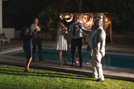 Celebrating by poolside, seniors raising glasses and having evening together. Celebration, toasting, leisure, retirement, elderly, lifestyleの写真素材
