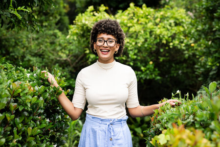 Smiling woman enjoying nature in lush garden, surrounded by vibrant greenery. relaxation, outdoors,...