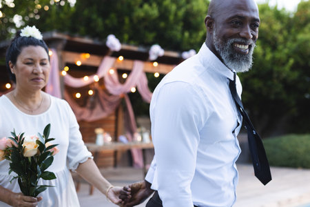 Holding hands, senior couple with flowers celebrating special occasion outdoors. Elderly, romance, celebration, togetherness, affection, intimacyの写真素材