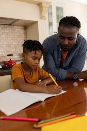 Father helping son with homework at kitchen table, both concentrating on task. Parenting, education, study, family, assistance, guidanceの写真素材