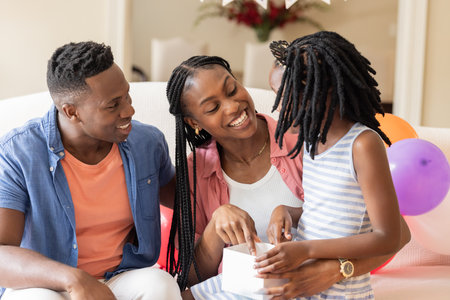 Celebrating birthday at home, African American family smiling and opening gift together. Celebration, joy, present, happiness, togetherness, festiveの写真素材