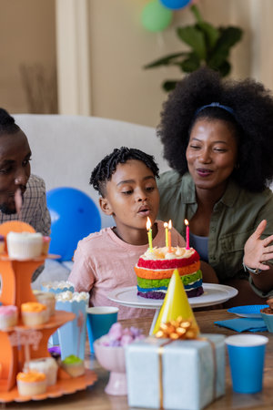 African American family celebrating birthday with child blowing out candles on cake. celebration, togetherness, tradition, happiness, joy, partyの写真素材
