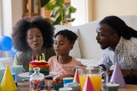 Celebrating birthday, African American family blowing out candles on colorful cake together....