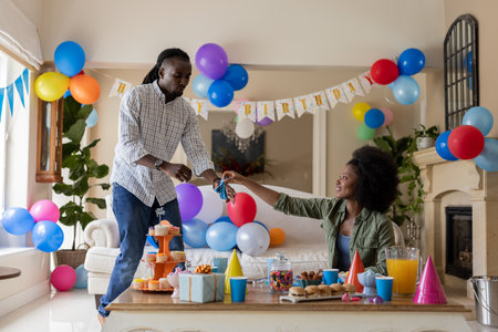 Decorating room with colorful balloons and snacks, African American couple celebrating birthday. Celebration, party, festive, decorations, joy, happinessの写真素材