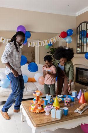 African American family celebrating birthday at home with balloons and party hats. Celebration, happiness, joy, togetherness, cheerful, funの写真素材