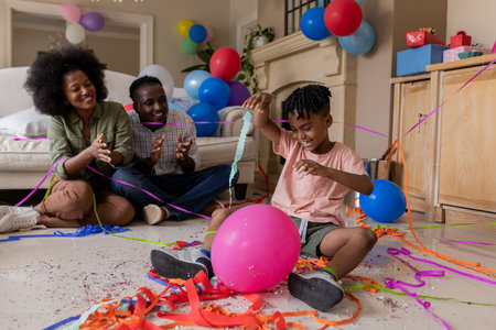 African American family celebrating birthday at home with balloons and streamers. Celebration, festive, party, colorful decorations, bonding, togethernessの写真素材
