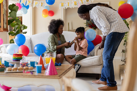 Celebrating birthday, family enjoying party with balloons and cake at home. Celebration, family time, happiness, decorating, tradition, gatheringの写真素材