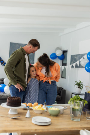 Family celebrating at home, smiling and embracing near decorated table with cake. Celebration, family gathering, party, happiness, togetherness, festiveの写真素材