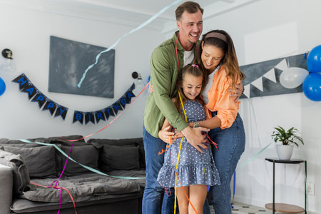 Family celebrating birthday at home, hugging and smiling with decorations around. Celebration, party, happiness, togetherness, bonding, joyfulの写真素材