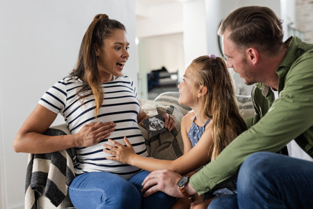 At home, daughter touching mother's pregnant belly, family bonding, smiling warmly. Pregnancy, love, motherhood, connection, warmth, expectingの写真素材