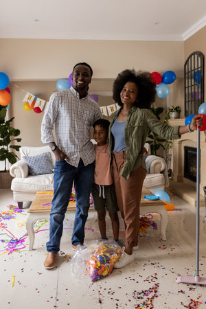 Family celebrating birthday at home, smiling with balloons and confetti on floor. Celebration, happiness, togetherness, joy, indoorsの写真素材