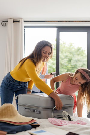 Mother and daughter packing suitcase together at home, preparing for vacation. Travel, family, tourism, leisure, bonding, tripの写真素材