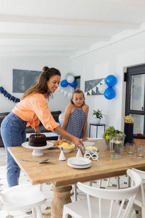 Mother and daughter preparing birthday table with cake and decorations at home. Family, celebration, togetherness, party, parent, festiveの写真素材