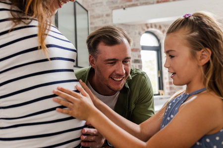 Smiling family bonding, young girl touching pregnant mother's belly at home. maternity, togetherness, love, pregnancy, happiness, childの写真素材