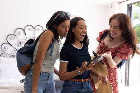 Laughing and sharing moment, three women gather around smartphone at home. They are enjoying each other's company, creating memories and strengthening their friendshipの写真素材