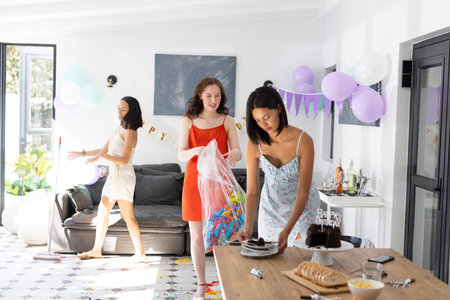 Preparing birthday celebration, three young women decorate bright living room with balloons. Friends are setting up cake and snacks, creating joyful party atmosphereの写真素材