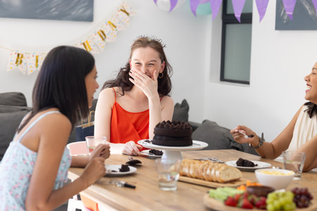 Laughing and enjoying cake, three young women gather at birthday celebration. Friendship and joy fill room as they share stories and delicious treatsの写真素材