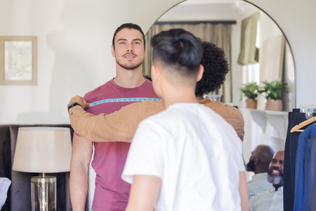 Groom getting measured for suit fitting, surrounded by friends, smiling warmly. Tailoring, friendship, preparation, wedding, celebration, menswearの写真素材