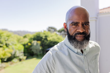 African American man standing outdoors, looking thoughtful in sunny garden setting. Contemplation, nature, reflection, sunshine, serenity, greeneryの写真素材