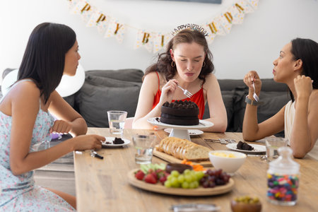Celebrating birthday, three young women enjoy chocolate cake at wooden table. Friends share laughter and conversation, creating joyful memories on this special occasionの写真素材