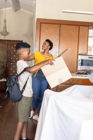 Mother and son unpacking cardboard box at home, smiling and enjoying time together. Family, moving, bonding, togetherness, happinessの写真素材