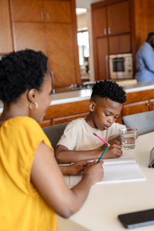 Mother helping son with homework at kitchen table, both focused and engaged. Family, education, studying, parenthood, tutoring, childhoodの写真素材