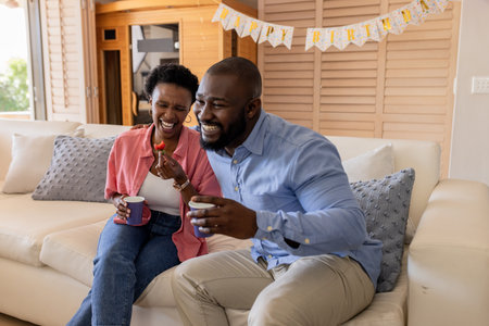 Celebrating birthday, happy couple enjoying coffee and laughter on cozy sofa. Celebration, anniversary, happiness, togetherness, relaxation, warmthの写真素材