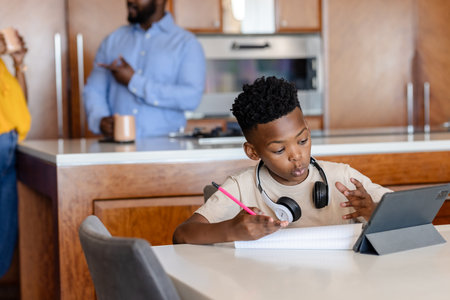 Young boy using tablet and writing in notebook at home, focused on learning. Studying, education, technology, homework, concentration, childの写真素材
