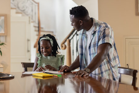 Father helping daughter with homework at home, both smiling and engaged. Parenting, family, bonding,...