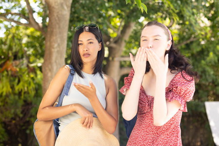 Posing, two young women enjoy sunny day outdoors. Friendship and joy radiate as they share playful...