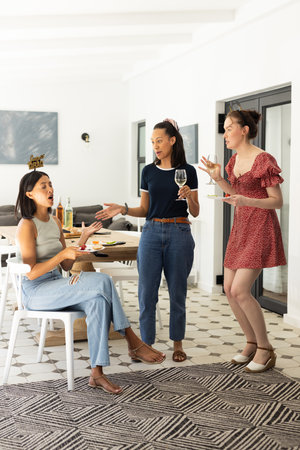 Engaging in animated conversation, three young women enjoy casual gathering at home. They are sharing laughter and stories, creating warm and lively atmosphereの写真素材