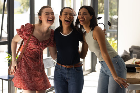 Laughing together, three young women enjoy sunny day indoors. Their joyful friendship creates warm and lively atmosphereの写真素材