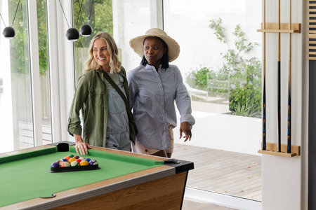 Two women enjoying leisure time by pool table in bright, modern room. recreation, friendship, billiards, relaxation, indoors, lifestyleの写真素材