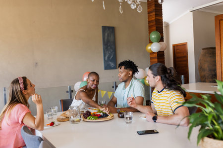 Friends enjoying conversation and sharing snacks at home during casual gathering. Friendship, celebration, party, relaxation, leisure, togethernessの写真素材