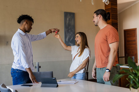 Real estate agent handing keys to excited couple in modern home. property, transaction, homebuying, homeowners, partnership, movingの写真素材
