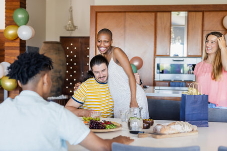 Friends celebrating at home, enjoying food and laughter around dining table. Celebration, gathering, dinner, meal, friendship, happinessの写真素材
