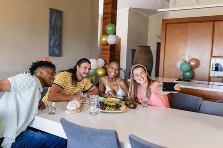 Friends gathering at home, smiling and taking selfie around dining table. Friendship, celebration, dinner party, togetherness, lifestyle, bondingの写真素材