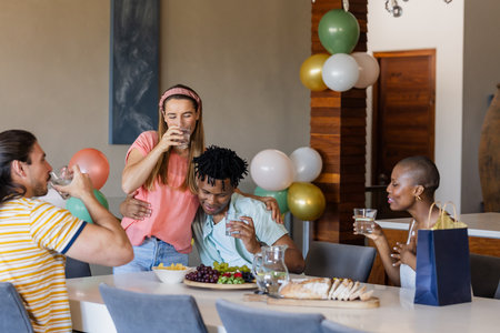 Friends celebrating at home, enjoying drinks and snacks around dining table. Celebration, friendship, gathering, party, casual, togethernessの写真素材