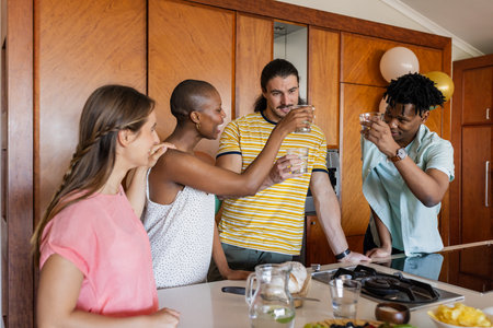 Friends toasting with drinks in modern kitchen, enjoying casual gathering together. Celebration,...