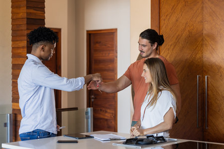 Diverse friends greeting with fist bump in modern office, smiling and connecting. Teamwork, collaboration, communication, workplace, friendship, diversityの写真素材