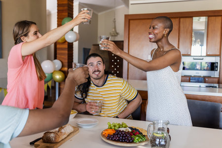 Friends celebrating at home, raising glasses around table with fruits and bread. Celebration, friendship, gathering, toast, cheers, hospitalityの写真素材