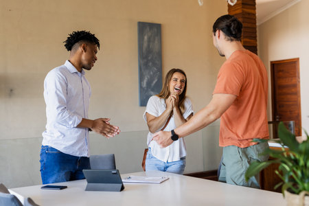 Friends celebrating success at home, smiling and clapping around tablet on table. Celebration, friendship, achievement, togetherness, technology, gatheringの写真素材